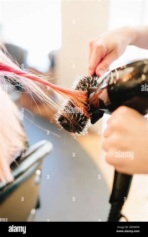 A Hair Stylist Blow Drying A Clients Long Straight Pink Hair Using A