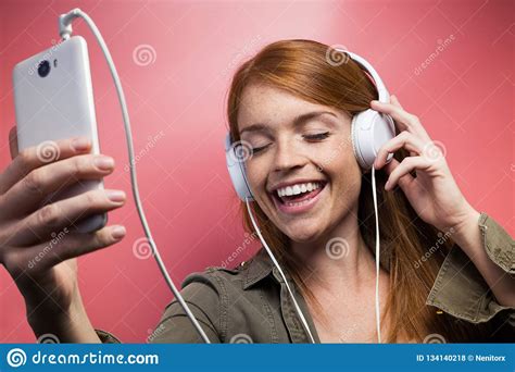 Beautiful Smiling Woman Listening To Music With Earphones Over Pink