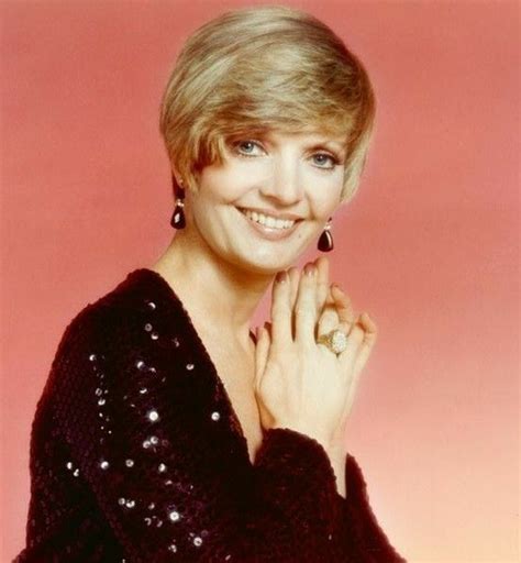 A Woman With Blonde Hair Wearing A Black Dress And Smiling At The Camera While Holding Her Hand