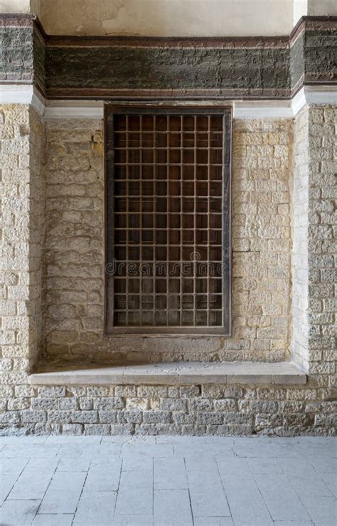 Recessed Wooden Window With Decorated Iron Grid Over Stone Bricks Wall