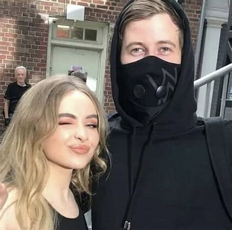 A Man And Woman In Black Hoodies Posing For The Camera With Their Arms