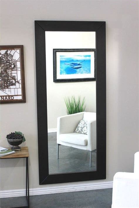 A Large Black Framed Mirror Sitting On Top Of A Wall Next To A White Chair