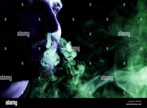 A Young Man Exhales A Cloud Of Colored Smoke Of Blue And Green Color On