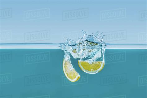Side View Of Fresh Lemon Slices Falling Into Water With Splashes