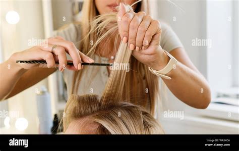 Female Hairdresser Making Hairstyle To Blonde Girl In Beauty Salon