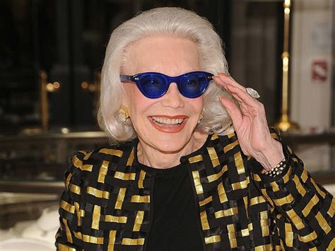An Older Woman Wearing Blue Sunglasses And Gold Jacket Smiling At The