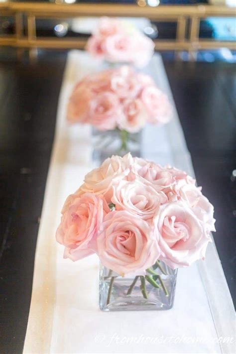 Three Vases Filled With Pink Roses Sitting On A Long White Table Cloth