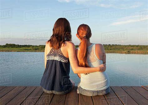 Caucasian Women Sitting On Wooden Dock Over Lake Stock Photo Dissolve