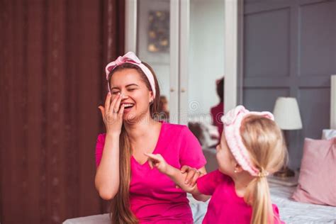 Girl And Her Mom Sitting On The Bed And Make Face Care Stock Photo