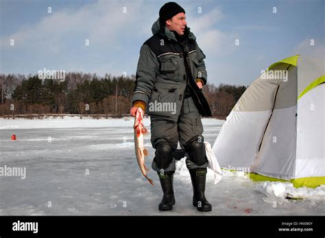 A Russian Man On Cold Winter Day As He Sits On Ice Fishing At A River