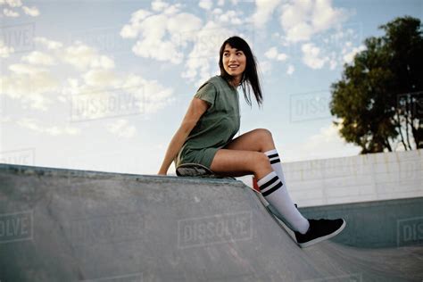 female skateboarder sitting on a ramp in skate park woman taking a break after skateboarding in