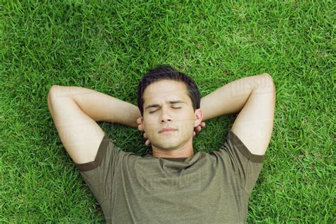 Young Man Lying On Grass With Hands Behind Head Eyes Closed High