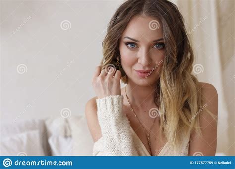 Blonde European Female Wearing Tender Fashionable Cardigan Sitting In Bright Modern Bedroom