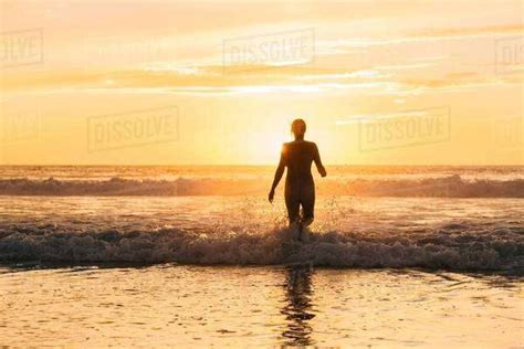 Rear View Of Mid Adult Nude Womans Silhouette Walking Into Ocean At
