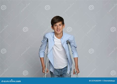 Teenage Boy With Injured Leg Using Crutches On Grey Background Stock