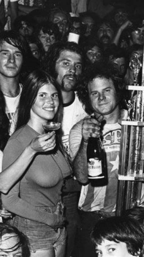 A Group Of People Standing Around Each Other At A Bar With Drinks In