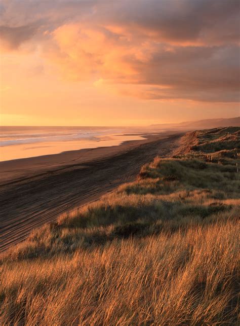 A Cloudy Sunset Over The Grassy Sand Dunes And Coastal Water At Port