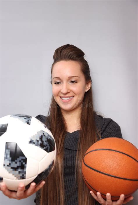 A Beautiful Smiling Girl Is Watching A Soccer Ball She Is Holding A Basketball In Her Other