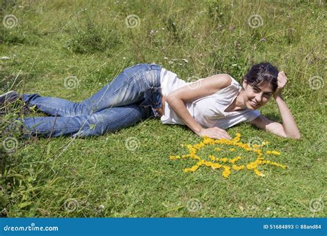 Young Woman Laying On A Meadow Close To Yellow Flowers In A Shape Of