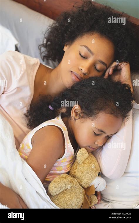 African American Mother And Daughter Sleeping Together On Bed In