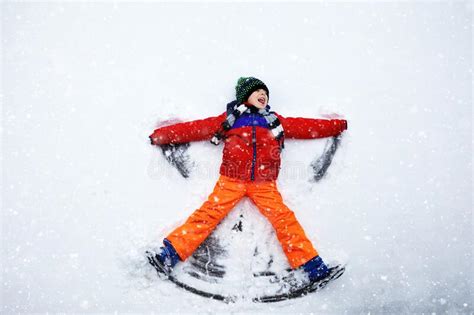 Cute Little Kid Boy In Colorful Winter Clothes Making Snow Angel