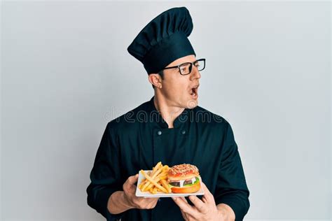 Handsome Young Man Chef Holding Burger With Fries Angry And Mad