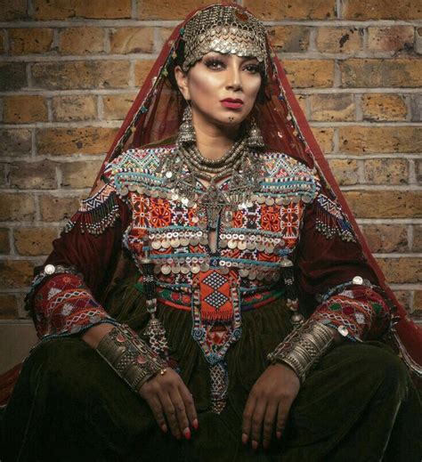 A Woman In An Elaborately Decorated Outfit Sits Against A Brick Wall With Her Hands On Her Hips