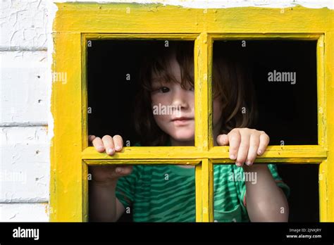 A little lad behind bars of a yellow window frame in an old playhouse