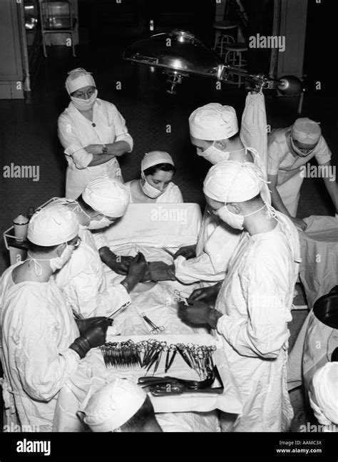 1930s Surgery Team Wearing White Gowns Caps And Masks In Hospital Operating Room Performing A