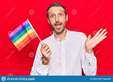 Young Handsome Man Holding Rainbow Lgbtq Flag Celebrating Achievement With Happy Smile And