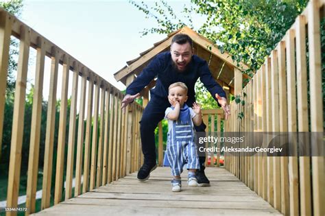 Father Chasing After Smiling Baby Boy In The Park High Res Stock Photo