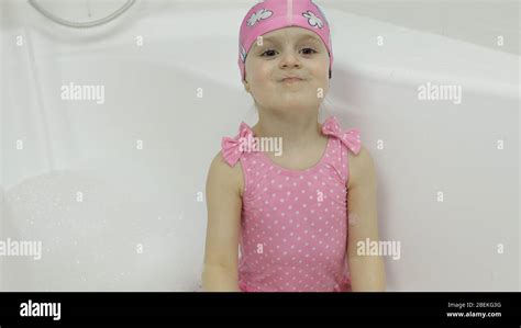 Attractive Four Years Old Girl Takes A Bath With Bath Foam In Pink Swimwear And Swimming Cap