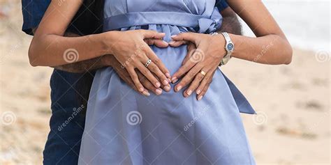 making a heart sign by the hands in front of the big belly of the pregnant wife couple stock