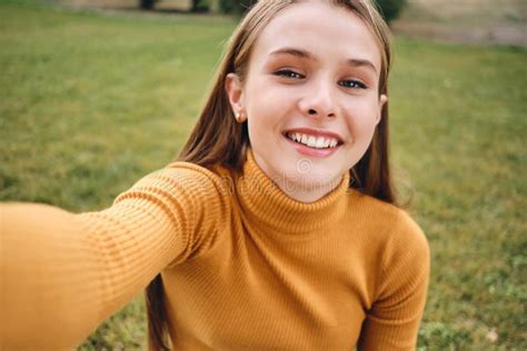 portrait of attractive smiling casual girl joyfully taking selfie in city park stock image