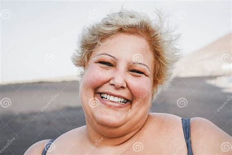 portrait of curvy woman smiling on camera wearing bikini with beach in background focus on
