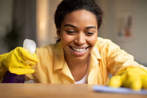 Happy African Woman Dusting Shelf With Detergent Cleaning At Home Stock