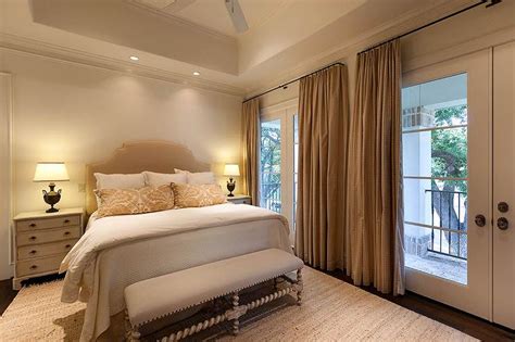 This master bedroom looks luxurious with wooden floor and immense windows covered with beige silk curtains. Beige Cottage Bedroom with French Doors - Cottage - Bedroom