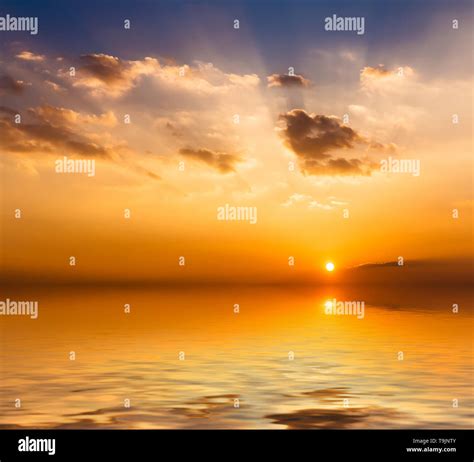 Dramatic Sky With Clouds And Sun Reflected In Water Surface Stock Photo