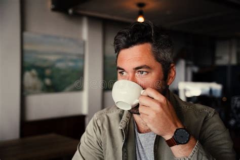 handsome man sipping coffee contently while sitting in fashionable cafe wearing watch stock
