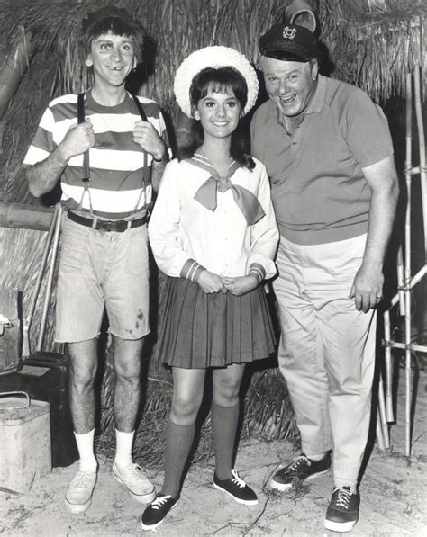 Two Men And A Woman Standing Next To Each Other In Front Of A Tiki Hut