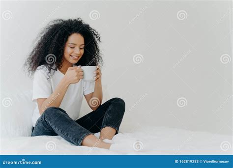 African American Woman Sips Hot Drink Poses In Bed Enjoys Good