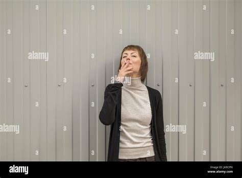 Mid Adult Woman Smoking Cigarette While Standing Against Wall Stock