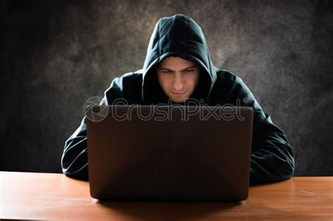 Hooded Computer Hacker Stealing Information With Laptop Stock Photo