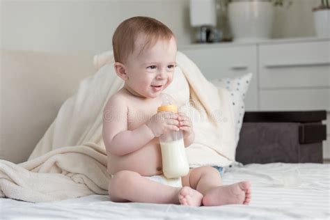 Baby Boy In Diapers Sitting On Bed And Holding His Bottle With M Stock
