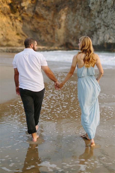 Young Couple Holding Hands And Strolling Along Beach Del Colaborador