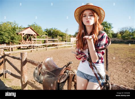 Pretty Redhead Cowgirl In Straw Hat Sending Air Kiss While Sitting On