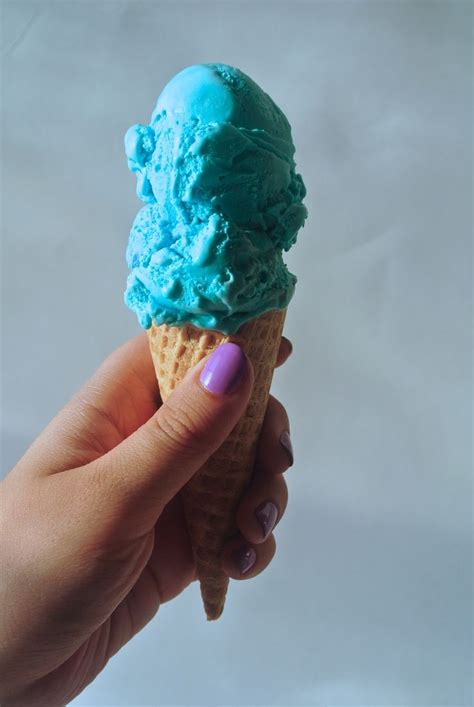 A Woman S Hand Holding An Ice Cream Cone With Blue Icing On It