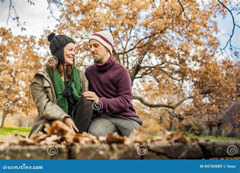 Lovely Young Couple Talking Sit In A Bench In The Park In Autumn Stock