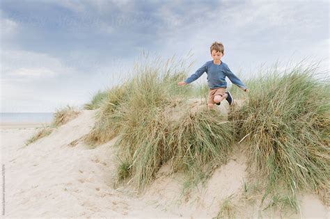 Boy Jumping Off Sand Dune On The Beach Del Colaborador De Stocksy