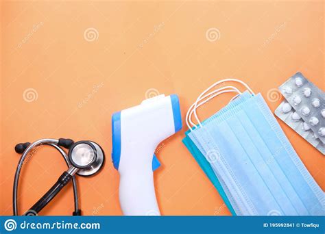 Surgical Masks Thermometer And Hand Sanitizer On Orange Background
